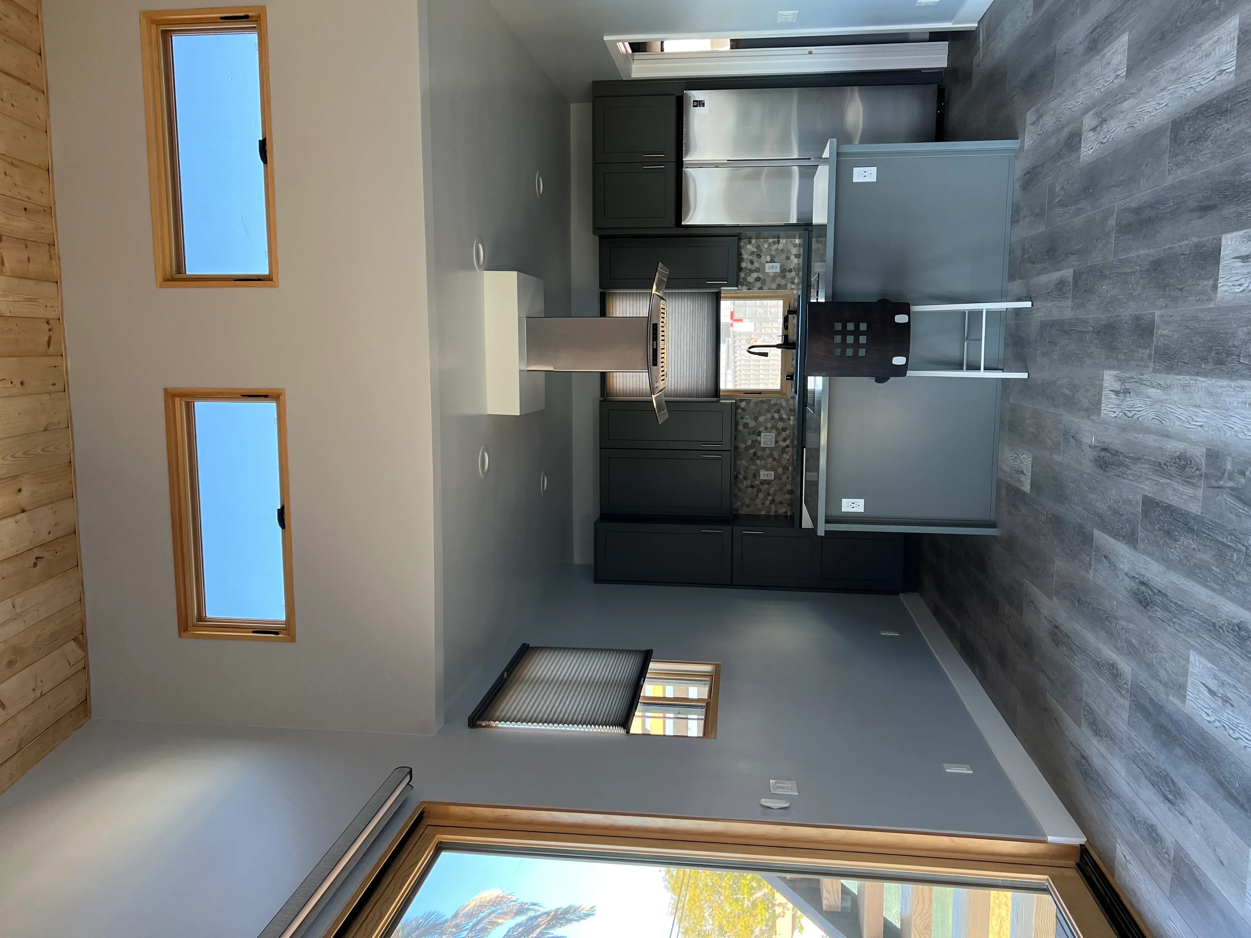 Kitchen and bathroom renovation with black cabinets, stainless steel appliances, gray tile flooring, and glass shower enclosure