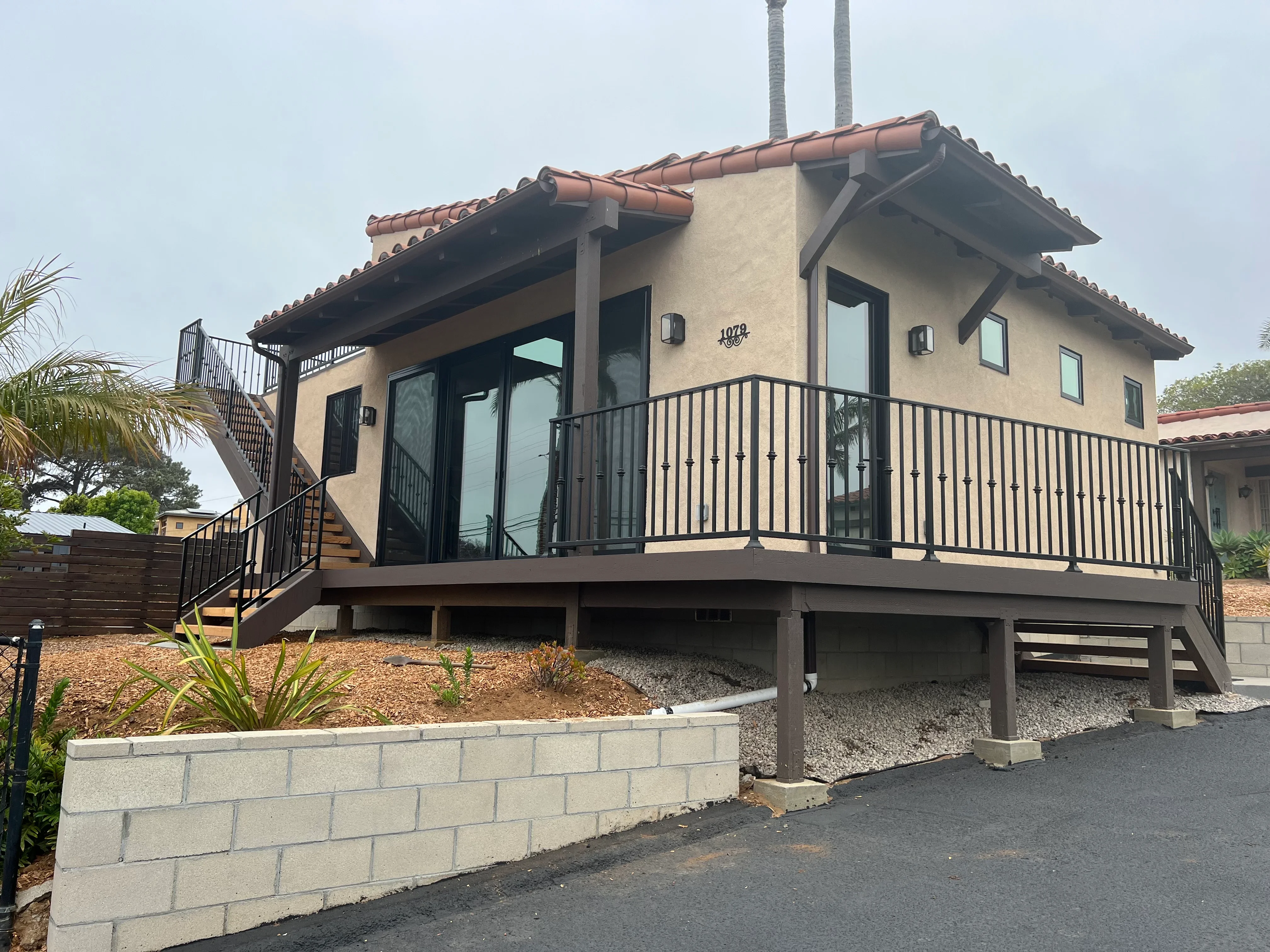 Spanish Colonial home with elevated composite deck, metal railings, concrete retaining wall, and stucco exterior