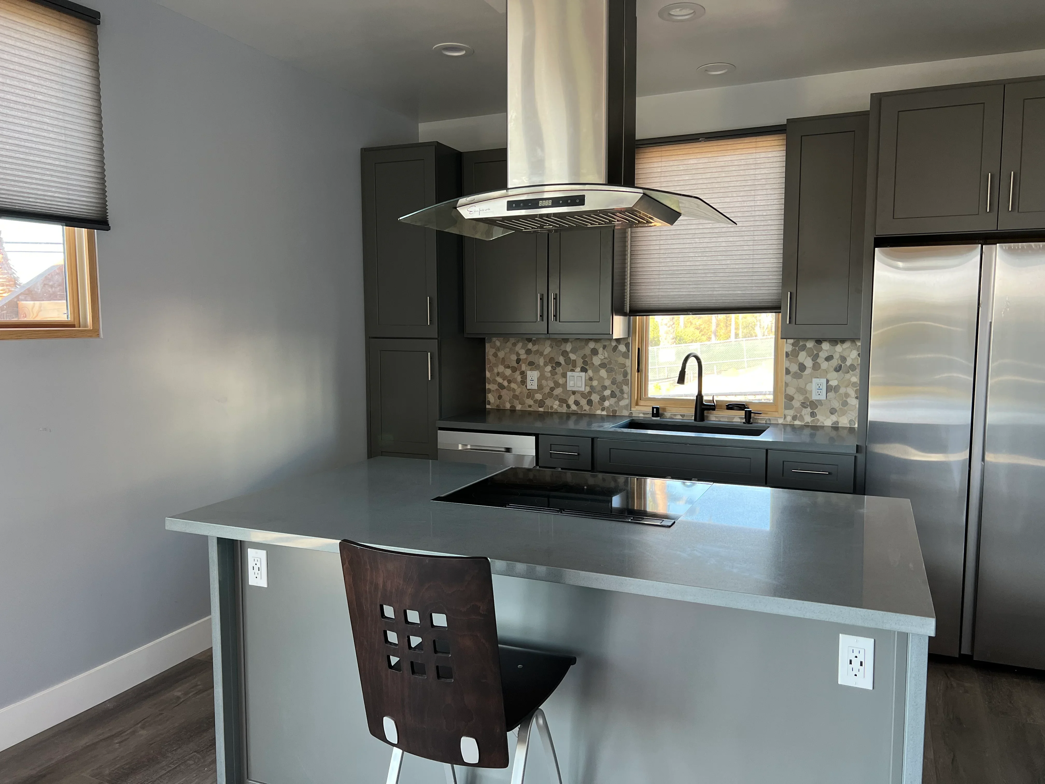 Modern kitchen with dark cabinetry, geometric tile backsplash, stainless steel appliances, and waterfall island